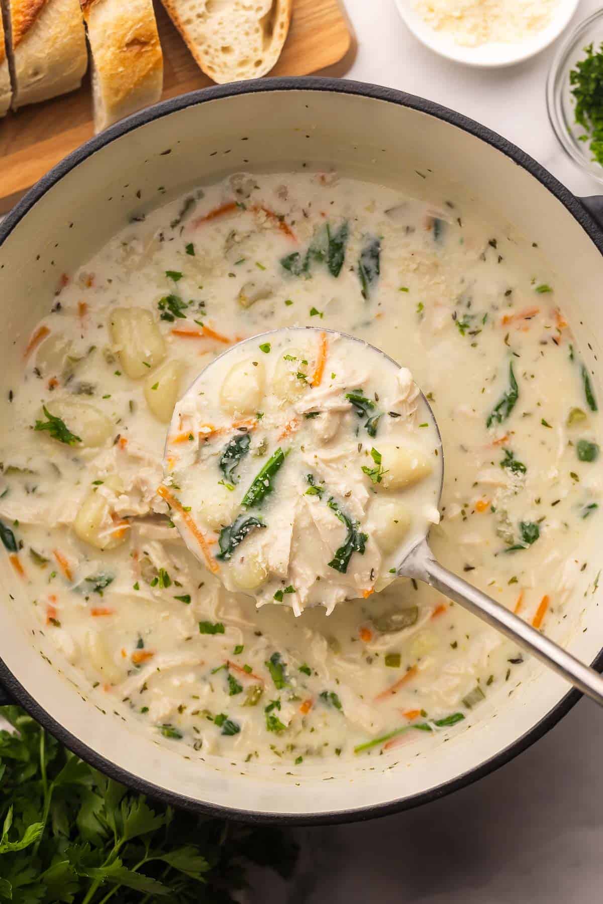 scooping chicken gnocchi soup out of pot with bread beside it.