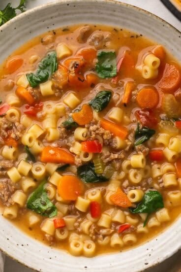 a large bowl of italian sausage soup with parsley beside it.