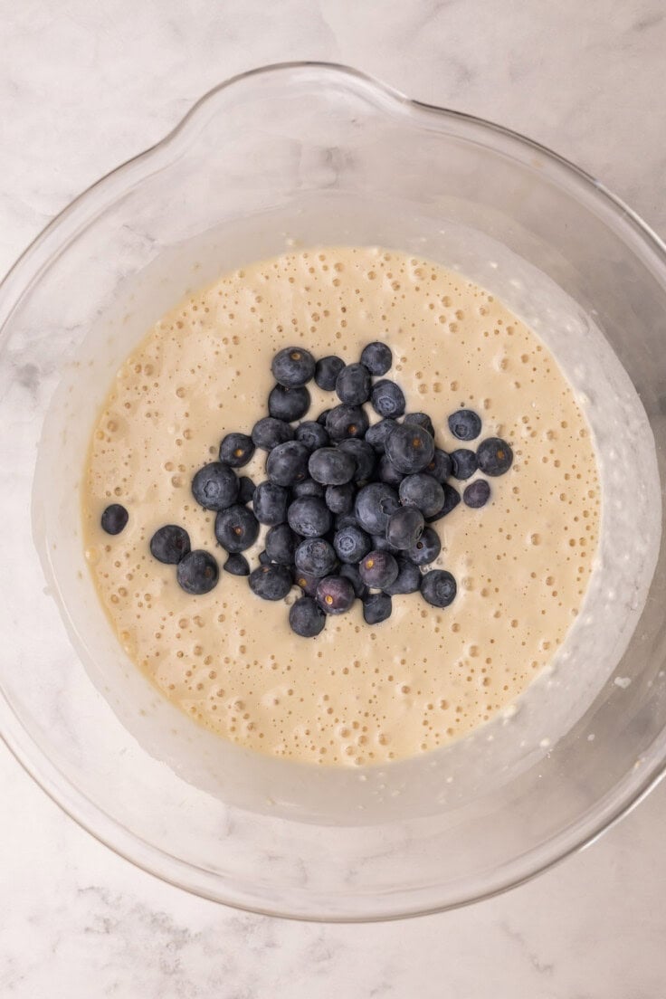 blueberries added to pancake batter in glass bowl.