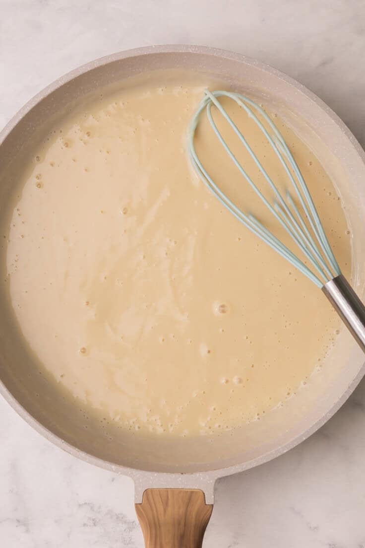 large pan with sauce and whisk in it.