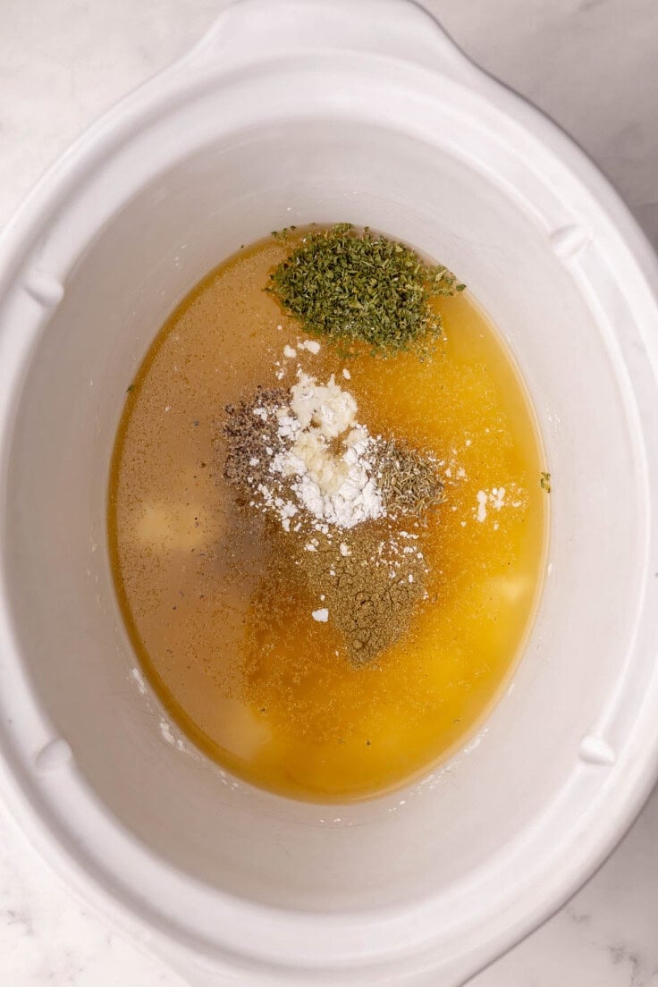 broth and other ingredients added into white crockpot.