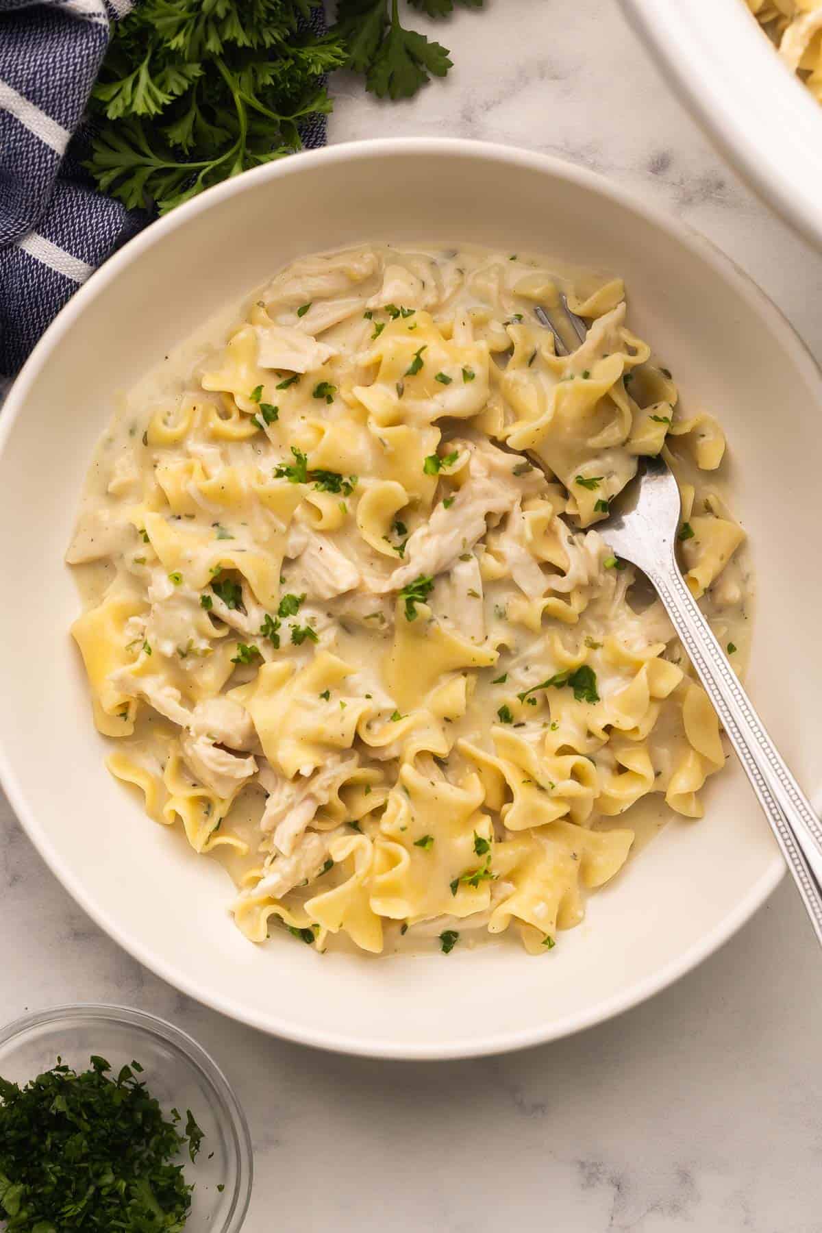 Crockpot Chicken and Noodles is a creamy, cozy slow cooker dinner with tender shredded chicken breast and egg noodles, made from scratch with no canned soup! #chicken #crockpot #dinner #recipe | dinner recipes | crockpot meals | slow cooker recipes | chicken breast recipes | comfort food | easy recipes | the recipe rebel a plate of chicken and noodles with a fork in it.