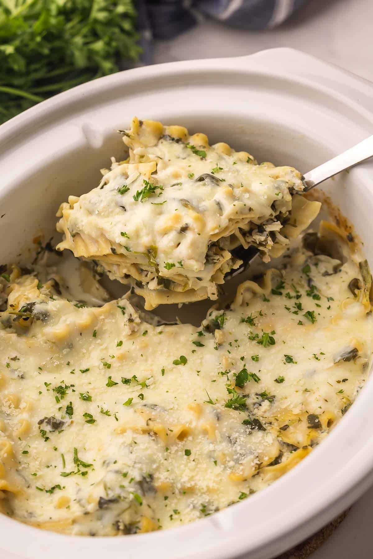 Crockpot White Chicken Lasagna is a creamy, cheesy slow cooker dinner with chicken, spinach and lasagna noodles all bubbling away in one pot! #dinner #recipe #slowcooker | slow cooker meals | crockpot recipes | chicken dinner | chicken breast | slow cooker meals | white lasagna a scoop of white chicken lasagna coming out of crockpot.