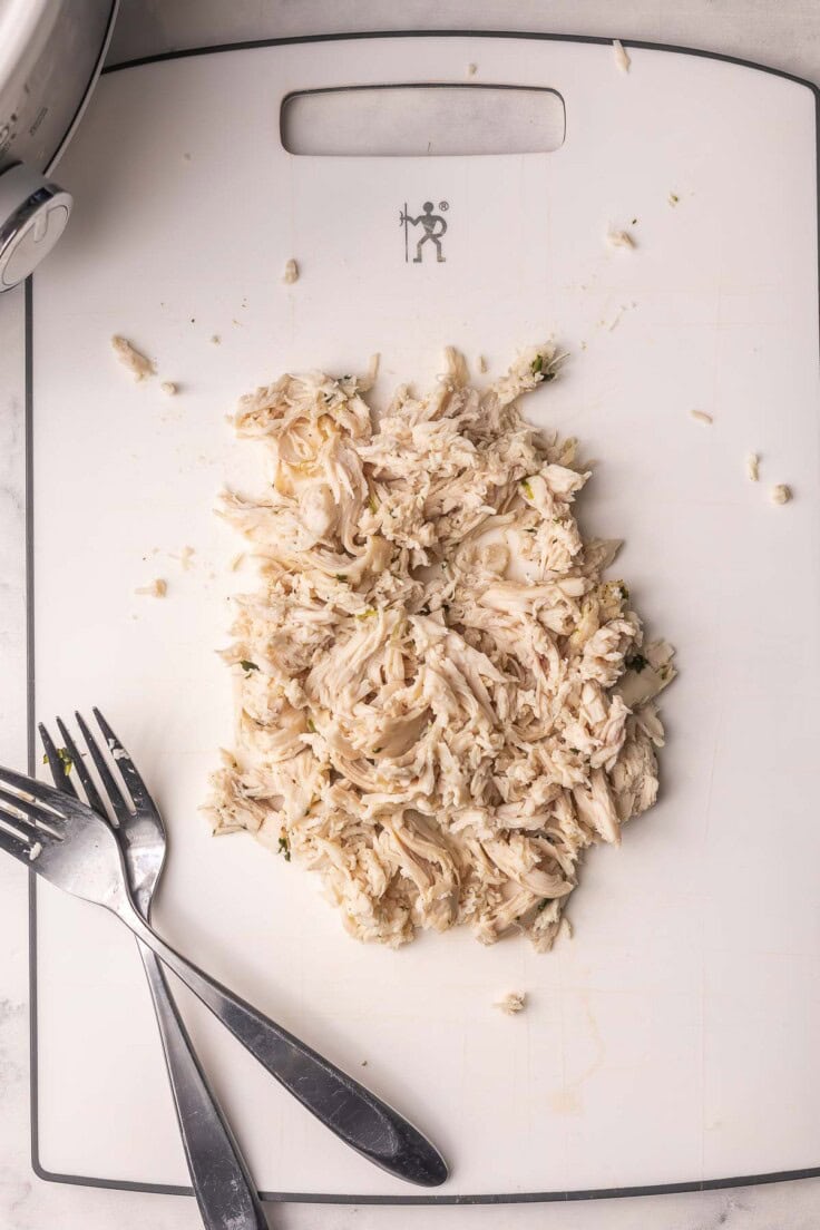 shredded chicken on a white cutting board with two forks.