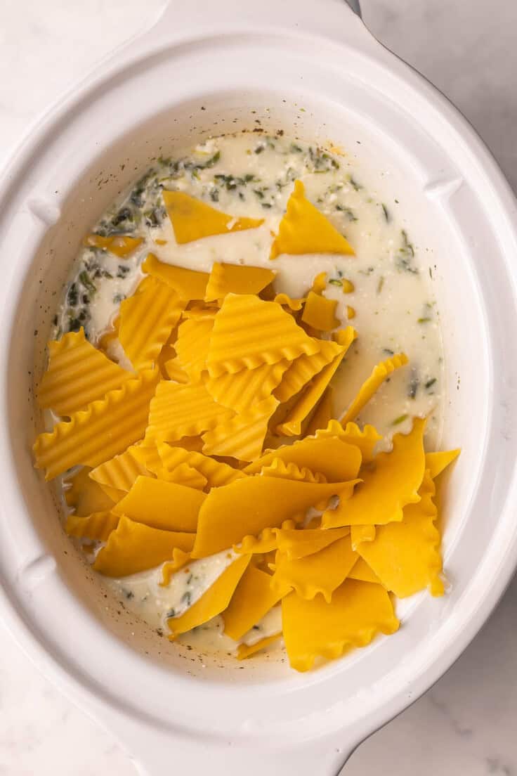 broken lasagna noodles added to other ingredients in white crockpot.
