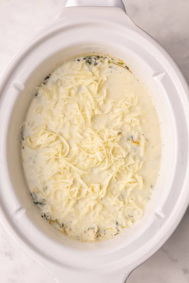 shredded mozzarella added to crockpot of white chicken lasagna.