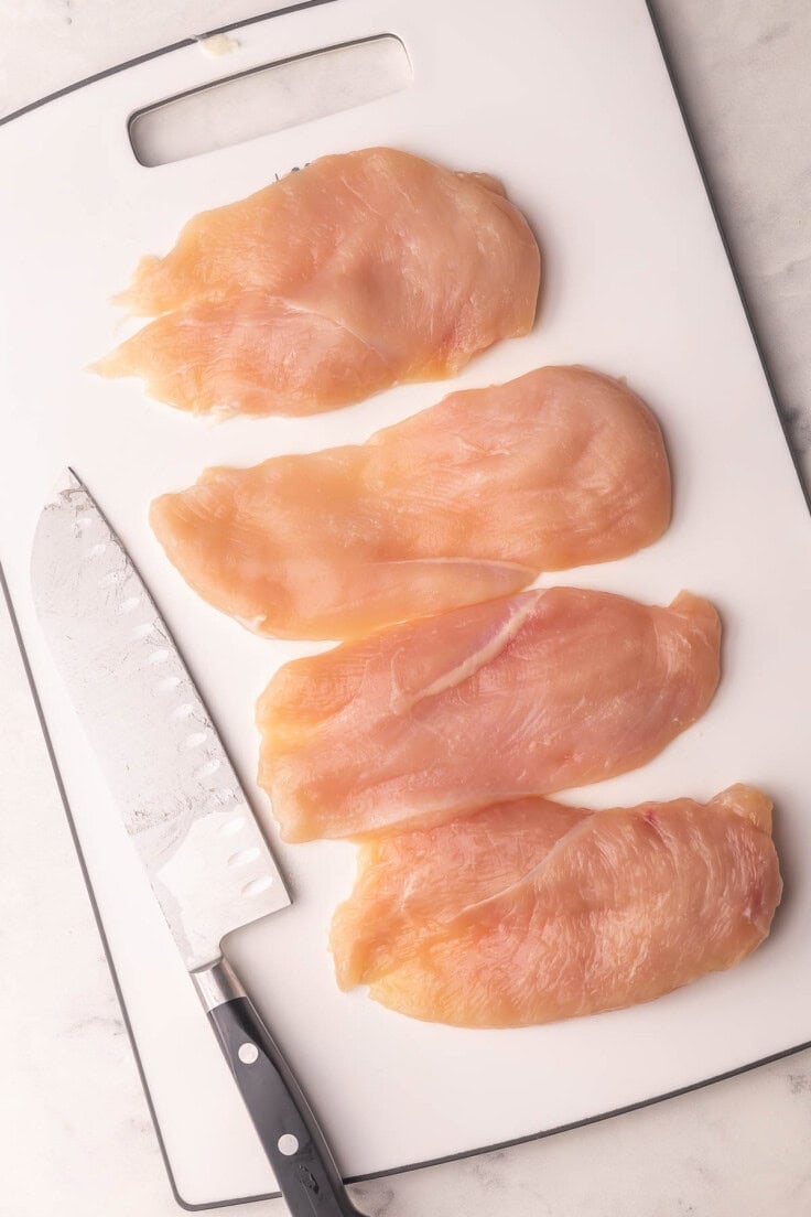 raw chicken breast on white cutting board with knife beside.