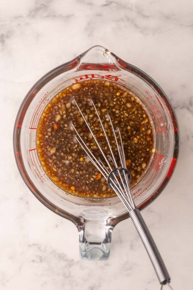 glass measuring cup with honey garlic sauce and whisk in it.
