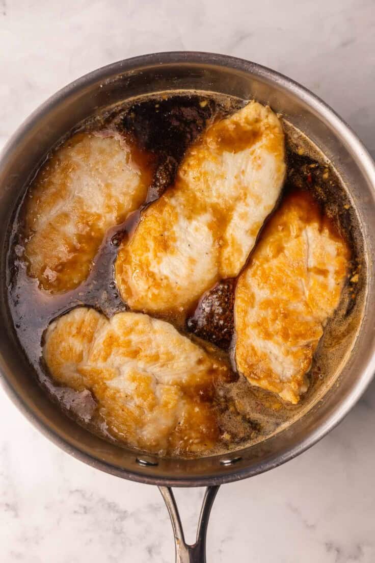 chicken in a pan full of honey garlic sauce.