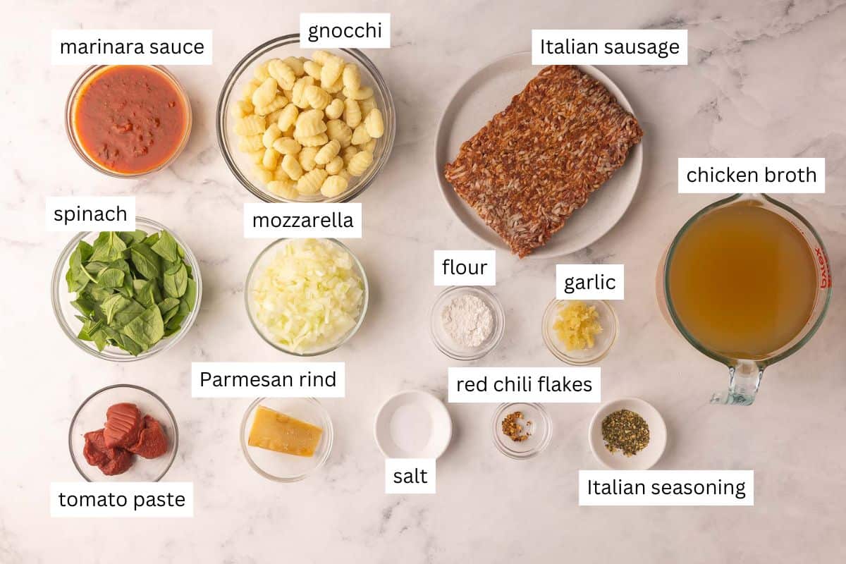 This Italian Sausage Gnocchi Soup will turn up the heat on those cold days. There is so much flavor in this soup with Italian sausage, tons of seasonings, and a parmesan rind, you can even add red pepper flakes for an extra kick! #soup #recipe | dinner recipes | soup recipe | italian sausage | gnocchi | dinner ideas ingredients needed for sausage gnocchi soup on a white background.