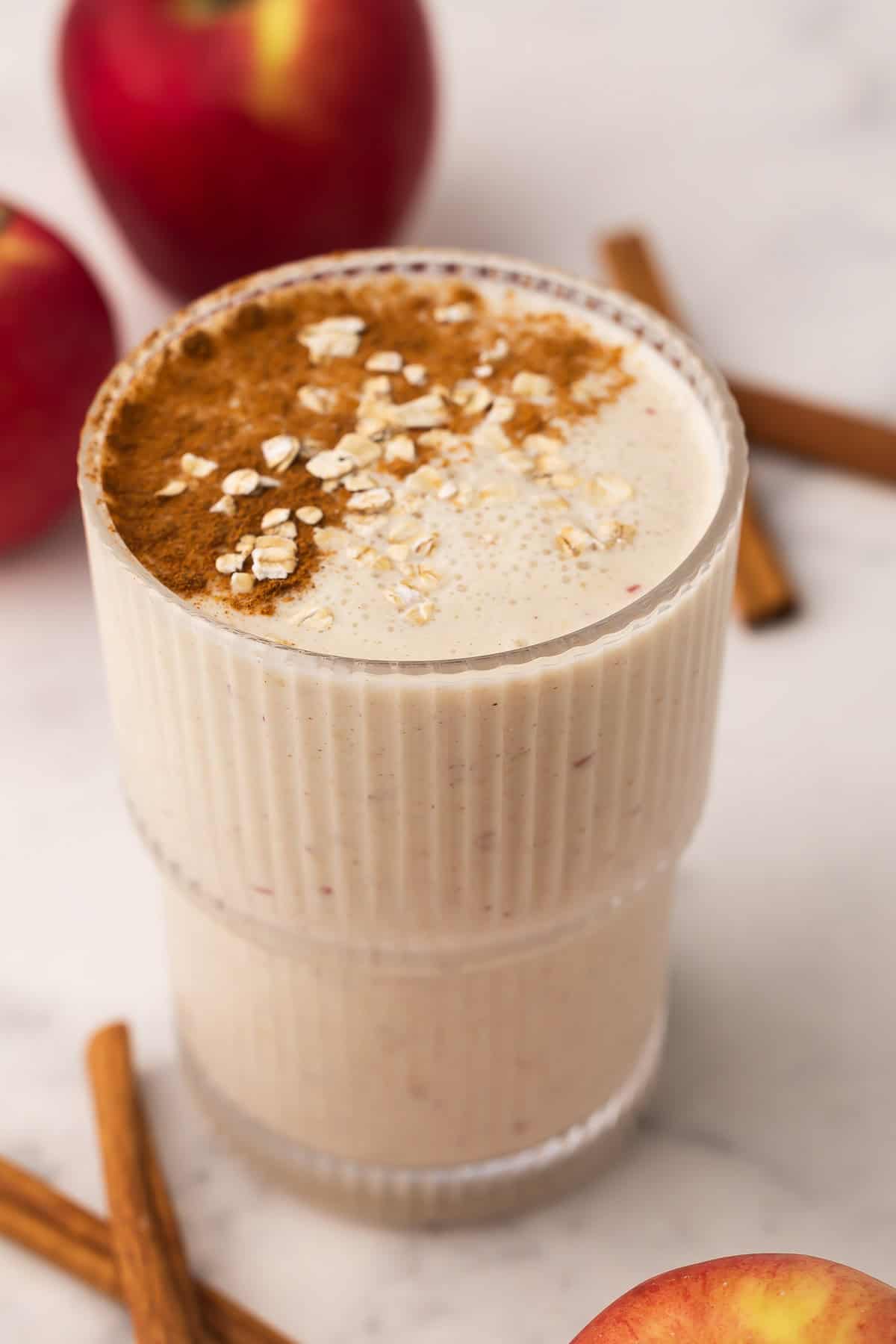 Apple Crisp Smoothie blends apple, oats, vanilla Greek yogurt, and cinnamon into a thick, on-the-go breakfast in 5 minutes, high in protein and fiber with real "apple crisp" flavor! #smoothie #drink #breakfast | smoothie recipe | drink recipes | apple smoothie | healthy smoothie | high fiber breakfast | oats | oatmeal smoothie | apple cinnamon glass cup of apple crisp smoothie with cinnamon sticks beside.