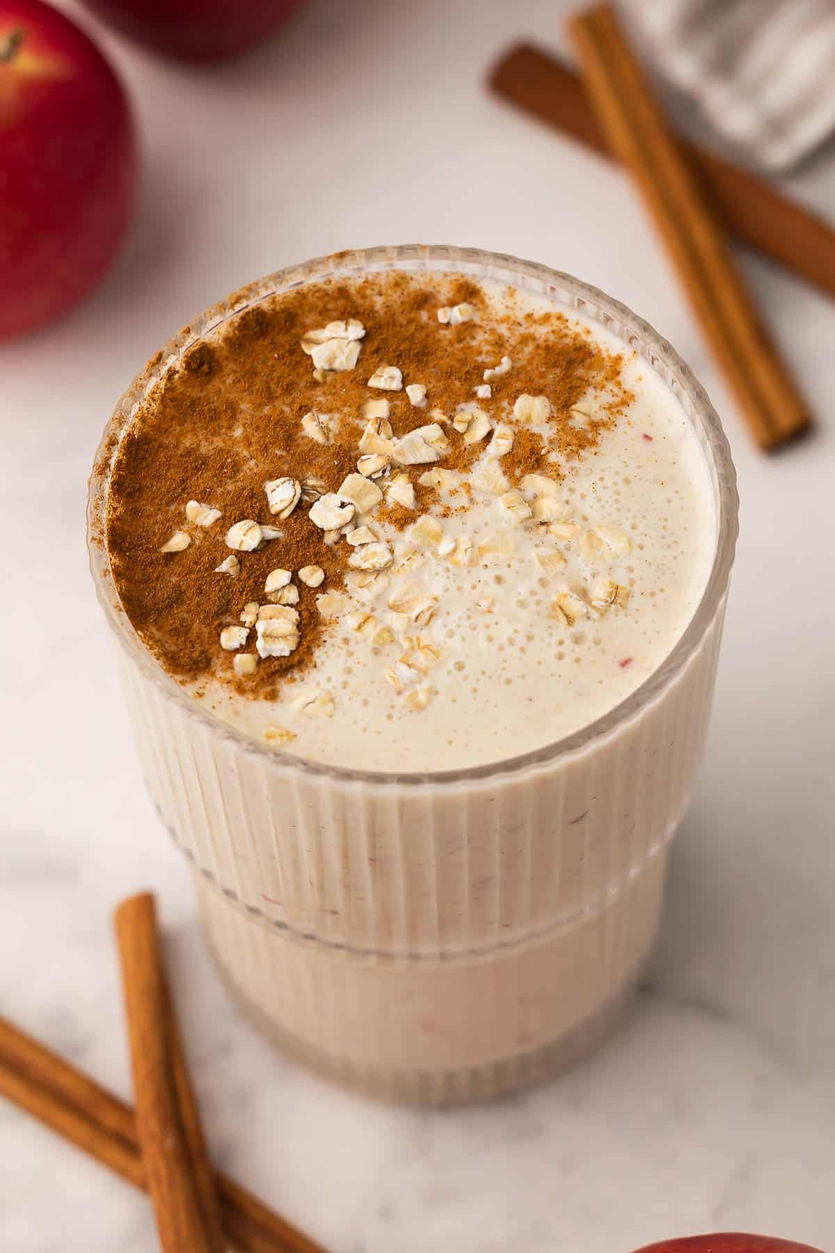 Apple Crisp Smoothie blends apple, oats, vanilla Greek yogurt, and cinnamon into a thick, on-the-go breakfast in 5 minutes, high in protein and fiber with real "apple crisp" flavor! #smoothie #drink #breakfast | smoothie recipe | drink recipes | apple smoothie | healthy smoothie | high fiber breakfast | oats | oatmeal smoothie | apple cinnamon large cup of apple crisp smoothie with an apple behind.
