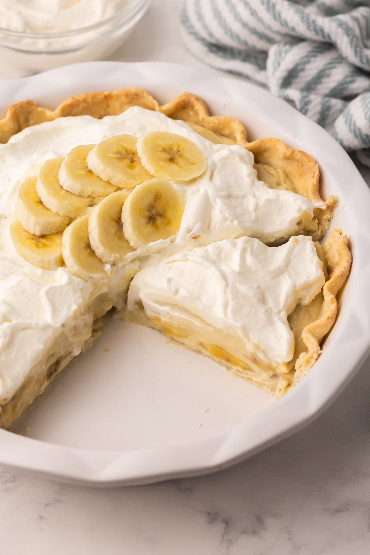 Banana Cream Pie is a classic, make-ahead cream pie with a flaky pie crust, thick vanilla custard, and lots of fresh banana slices, finished with a big cloud of homemade whipped cream! #banana #dessert #easter | easter dessert recipes | easy dessert recipes | homemade pie recipes | banana recipes | easter recipes | spring desserts | custard a slice of banana cream pie in pie pan.
