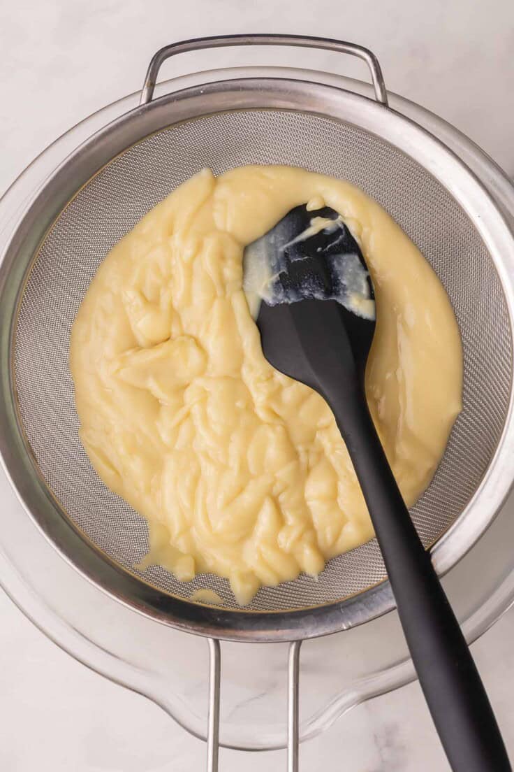 banana cream filling in strainer with black spatula.
