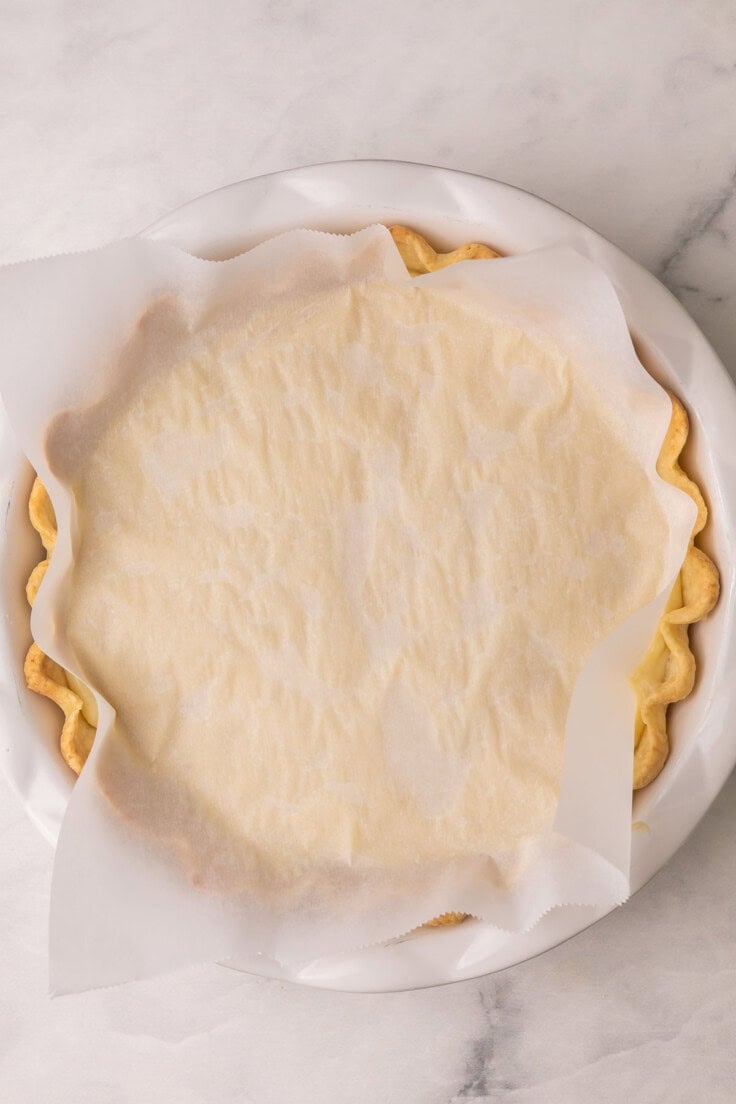 pie crust in a pan with a piece of parchment on top.