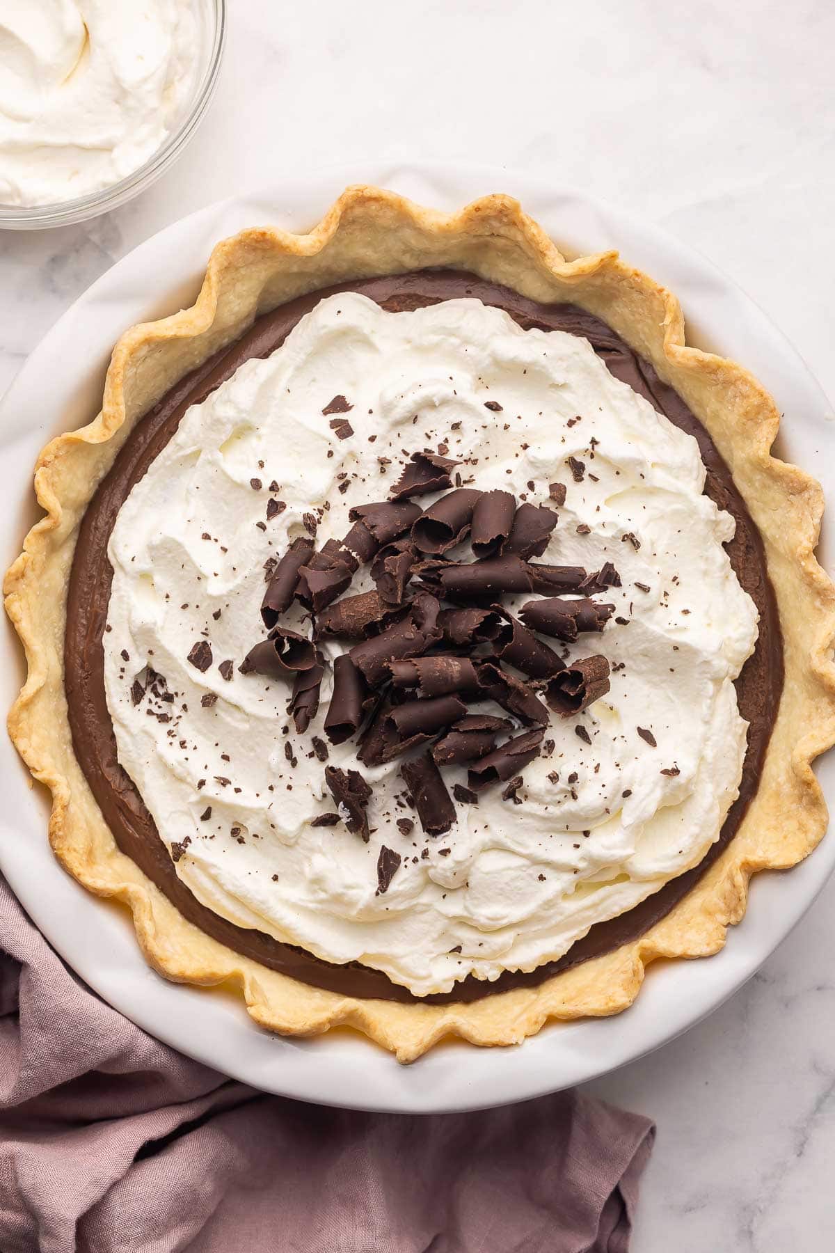 Chocolate Cream Pie is made with a flaky homemade pie crust, thick from-scratch chocolate custard, and a generous layer of homemade whipped cream (chocolate shavings encouraged)! It's the perfect Easter dessert! #chocolate #dessert #recipe | easter dessert recipes | easy desserts | homemade pie | chocolate dessert | homemade pie crust | holiday pies | holiday dessert a pan full of chocolate cream pie with whipped cream and chocolate curls on top.
