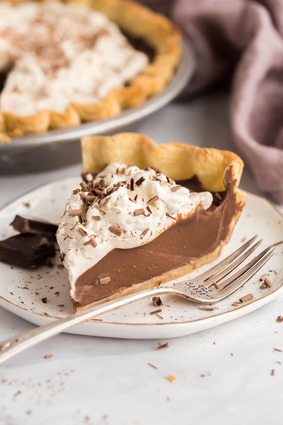 Chocolate Cream Pie is made with a flaky homemade pie crust, thick from-scratch chocolate custard, and a generous layer of homemade whipped cream (chocolate shavings encouraged)! It's the perfect Easter dessert! #chocolate #dessert #recipe | easter dessert recipes | easy desserts | homemade pie | chocolate dessert | homemade pie crust | holiday pies | holiday dessert a slice of chocolate cream pie and a fork on a plate.