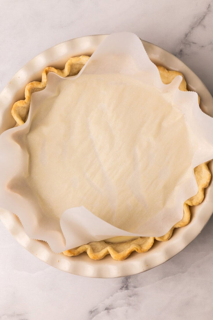 a baked pie crust in a pan with a piece of parchment over top.
