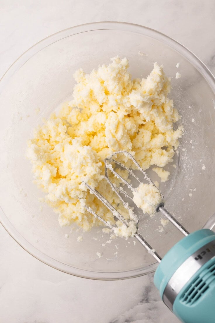 butter and sugar mixed in glass bowl with mixer beside.