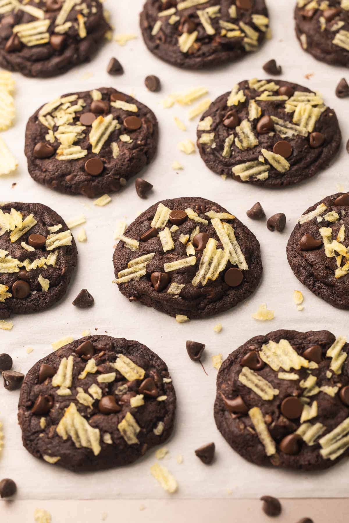 Double Chocolate Potato Chip Cookies are rich, fudgy chocolate cookies packed with chocolate chips and salty potato chips. No need to chill the dough, and they're ready in 25 minutes! #cookie #cookies #chocolate | chocolate cookies | sweet and salty | cookie recipes | baking recipes | easy dessert recipes | double chocolate potato chips cookies on parchment paper.