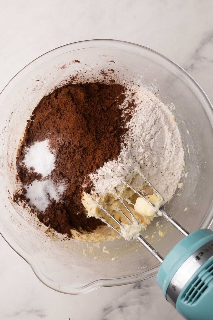 cocoa and other ingredients added to glass mixing bowl with mixer beside.