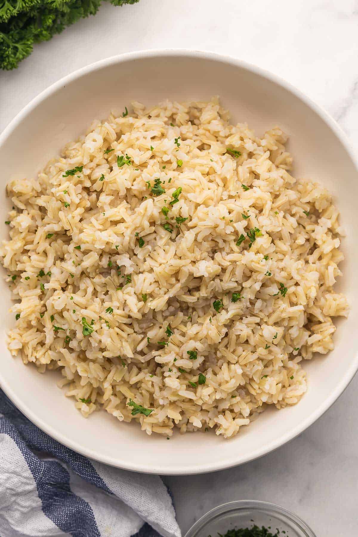 Learn How to Cook Brown Rice with this easy stovetop method for fluffy, tender rice every time. It’s simple, reliable, and great for meal prep! #recipe #rice #sides | easy recipes | side dish recipes | how to cook rice | brown rice recipe | long grain brown rice | easy recipes | dinner ideas a bowl of cooked brown rice with parsley beside.