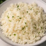 square image of cooked rice in a grey and white bowl with parsley on top.