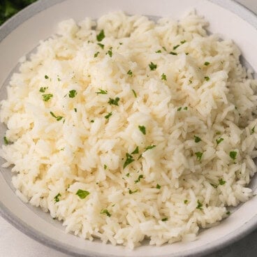 square image of cooked rice in a grey and white bowl with parsley on top.