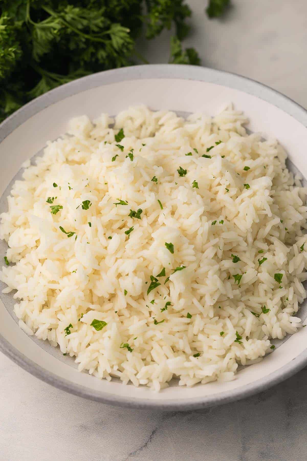 How To Cook Rice is a 20-minute, foolproof method for fluffy long-grain rice using a pasta-style boil, quick strain, and steam finish. No sticky pot! #rice #sidedish #dinner | side dish recipes | easy sides | how to make rice | how to cook white rice | long grain rice | foolproof rice | easy rice recipe cooked long grain rice in a grey and white bowl with parsley on top.