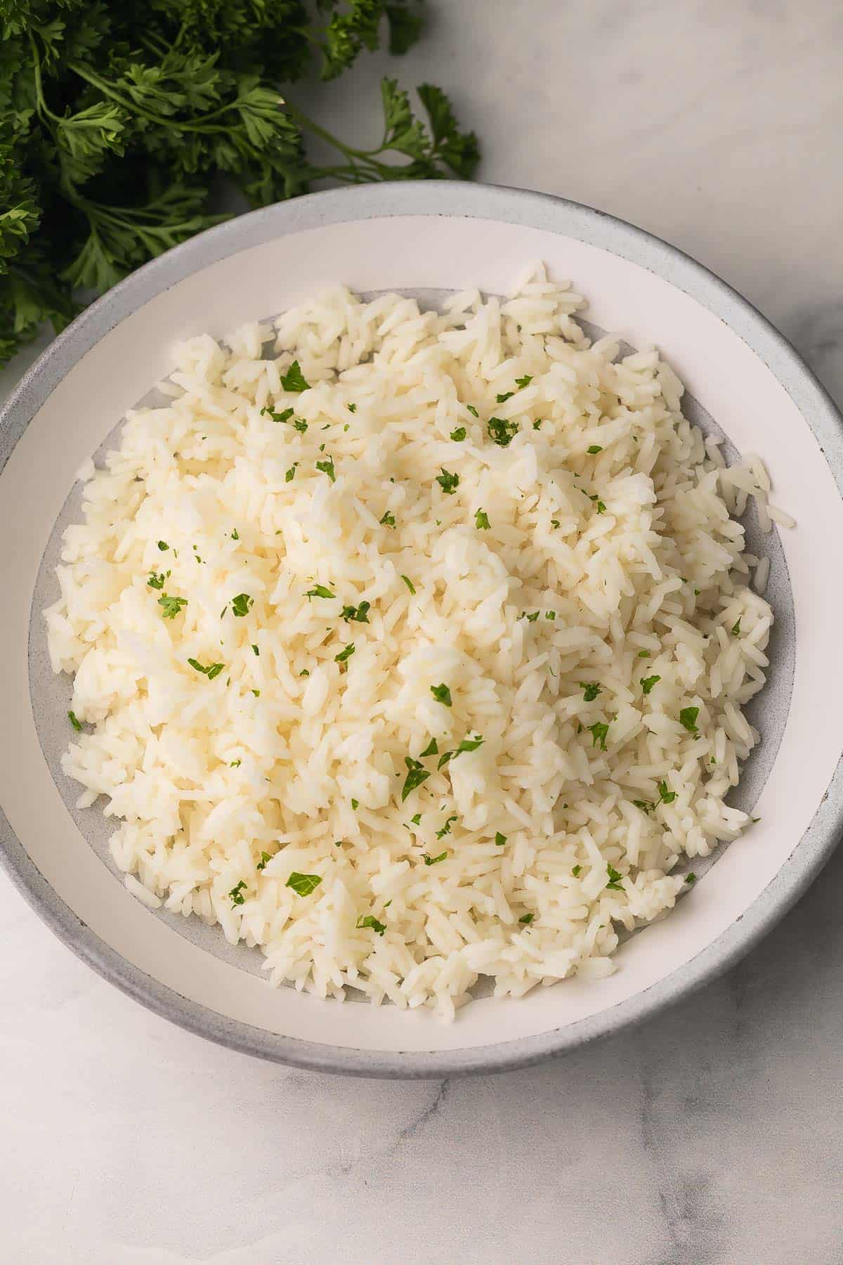 How To Cook Rice is a 20-minute, foolproof method for fluffy long-grain rice using a pasta-style boil, quick strain, and steam finish. No sticky pot! #rice #sidedish #dinner | side dish recipes | easy sides | how to make rice | how to cook white rice | long grain rice | foolproof rice | easy rice recipe overhead image of perfectly cooked white rice in white and grey bowl.