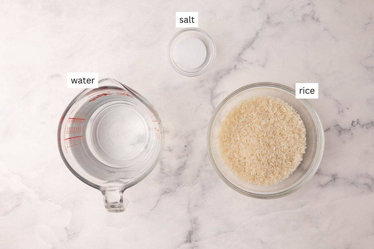 How To Cook Rice is a 20-minute, foolproof method for fluffy long-grain rice using a pasta-style boil, quick strain, and steam finish. No sticky pot! #rice #sidedish #dinner | side dish recipes | easy sides | how to make rice | how to cook white rice | long grain rice | foolproof rice | easy rice recipe ingredients needed to cook long grain white rice on a white marble background.