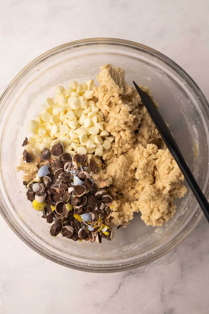 chocolate chips and chopped mini eggs added to dough in glass bowl.