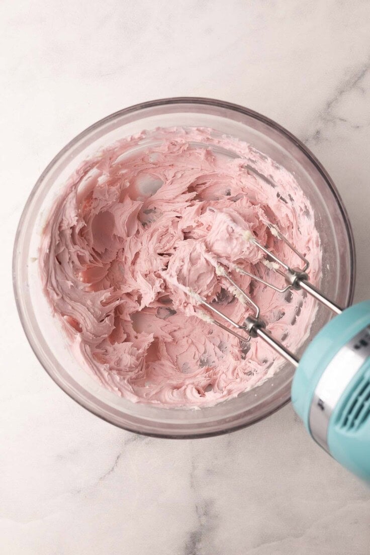 glass mixing bowl with pink frosting inside.