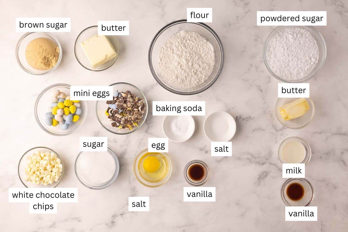 Make this Easter Mini Egg Cookie Cake in 30 minutes, packed with Mini Eggs and white chocolate, finished with pretty pastel buttercream swirls! An easy Easter dessert that disappears quickly. #easter #dessert #cookie | cookie recipes | cookie cake | skillet cookie | easter cookies | easter cake | easter recipes | mini egg recipes | easter eggs | chocolate chip cookie ingredients needed for mini egg cookie cake in bowls.