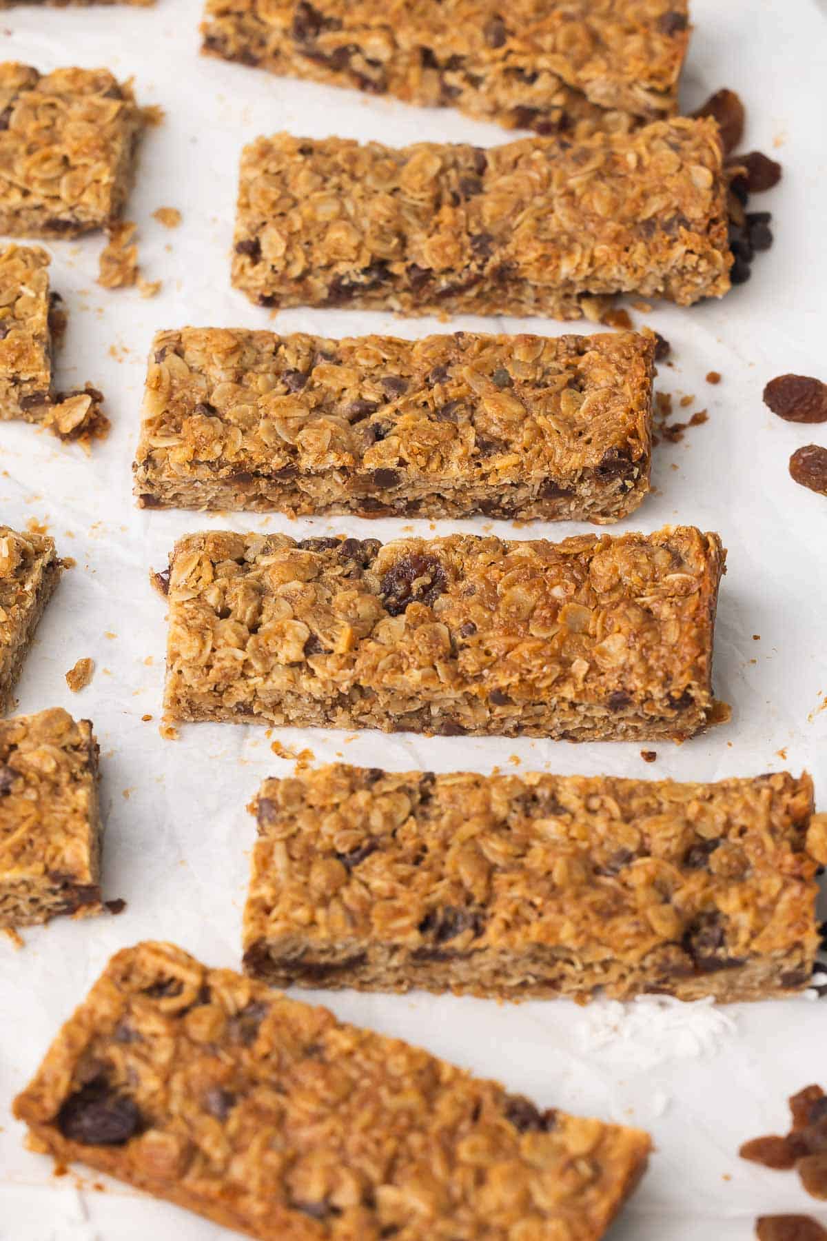 Peanut Butter Granola Bars bake up thick and chewy, loaded with creamy peanut butter, oats, coconut, raisins, and mini chocolate chips. The perfect on-the-go snack or breakfast, ready in 30 minutes! #breakfast #baking #recipe #easyrecipe | easy recipes | breakfast recipes | granola bar recipes | high fiber | high protein | kids snacks | lunch box snacks | oats peanut butter granola bars sliced on parchment paper.