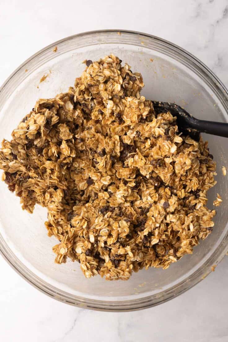 glass mixing bowl with mixed peanut butter granola bar ingredients.