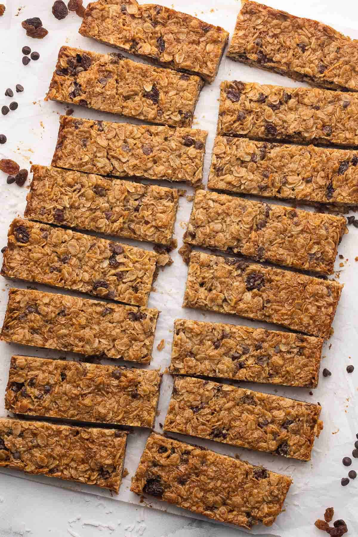 Peanut Butter Granola Bars bake up thick and chewy, loaded with creamy peanut butter, oats, coconut, raisins, and mini chocolate chips. The perfect on-the-go snack or breakfast, ready in 30 minutes! #breakfast #baking #recipe #easyrecipe | easy recipes | breakfast recipes | granola bar recipes | high fiber | high protein | kids snacks | lunch box snacks | oats overhead view of peanut butter granola bars on parchment paper.
