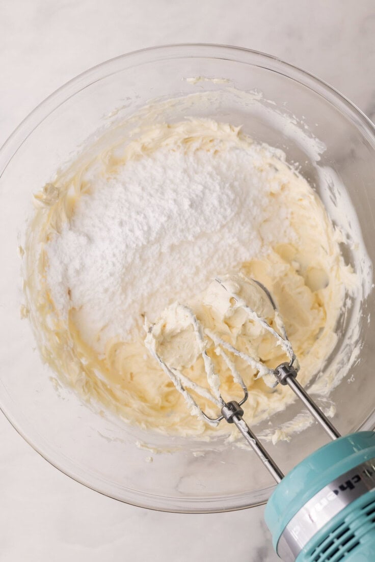 powdered sugar added to glass bowl with mixer beside.