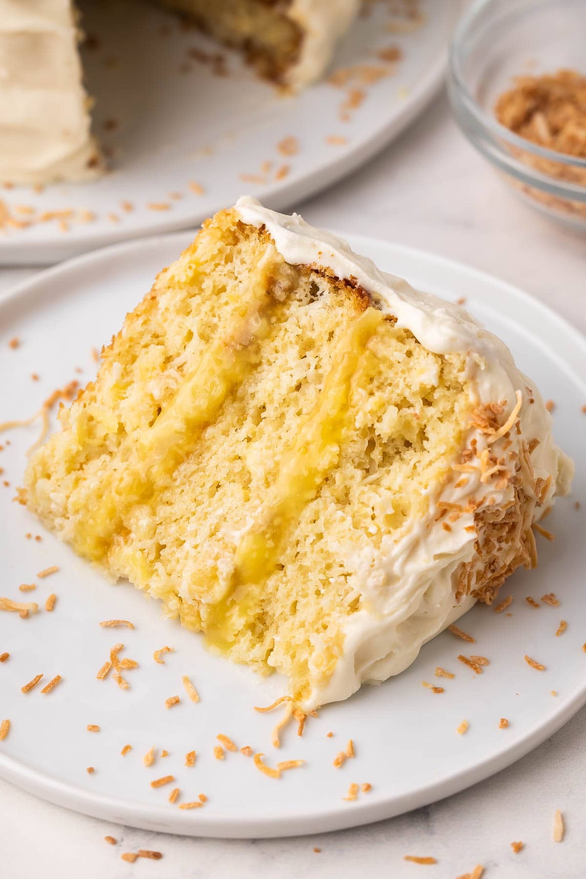 a slice of pineapple coconut cake on a white plate topped with toasted coconut.