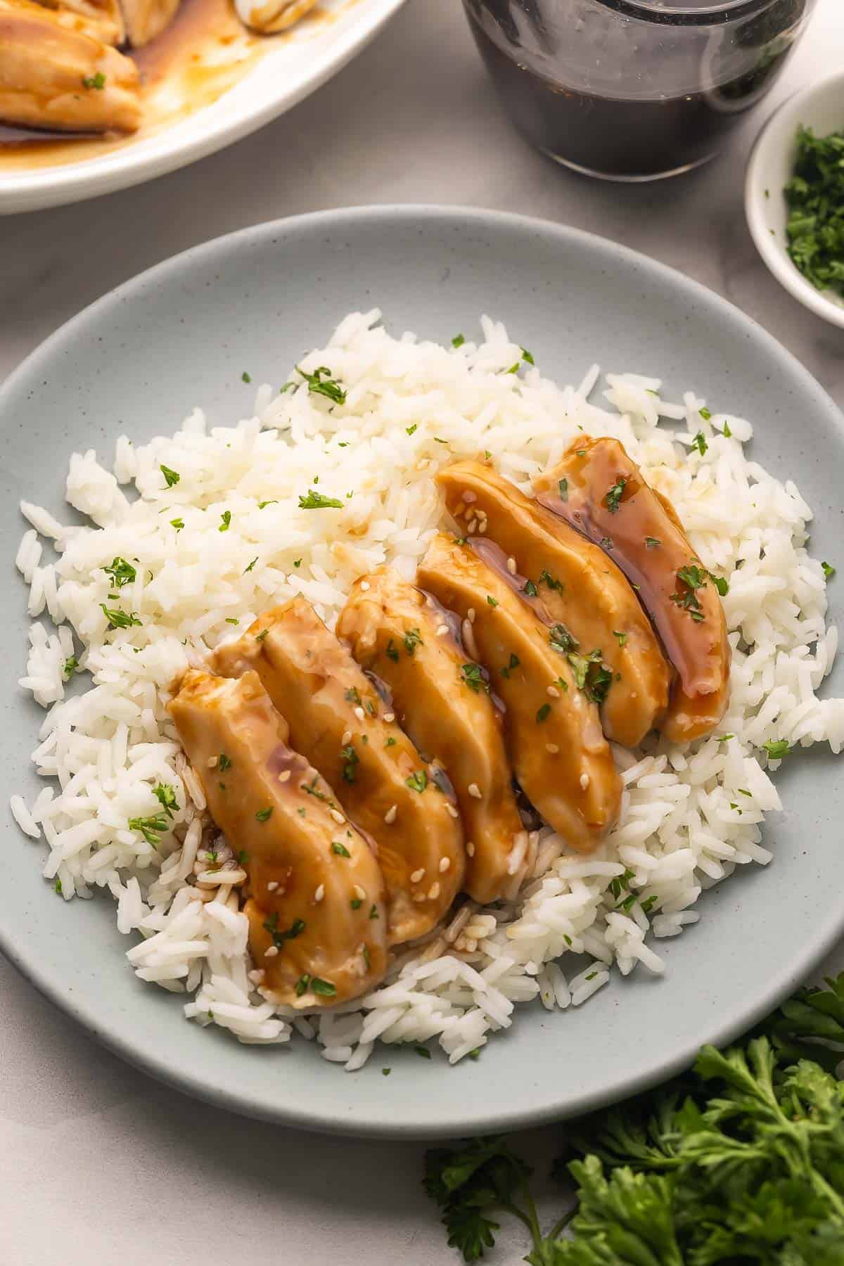 Slow Cooker Coconut Chicken cooks up tender in creamy coconut milk, then gets tossed in a sticky sweet-heat sauce. Serve it over rice or noodles for a bold, easy dinner! #slowcooker #dinner #recipe | chicken recipes | chicken breast | chicken dinner | dinner ideas | dinner recipes | slow cooker meals | crockpot chicken | easy dinners a blue plate filled with rice and sliced sweet and spicy coconut chicken.