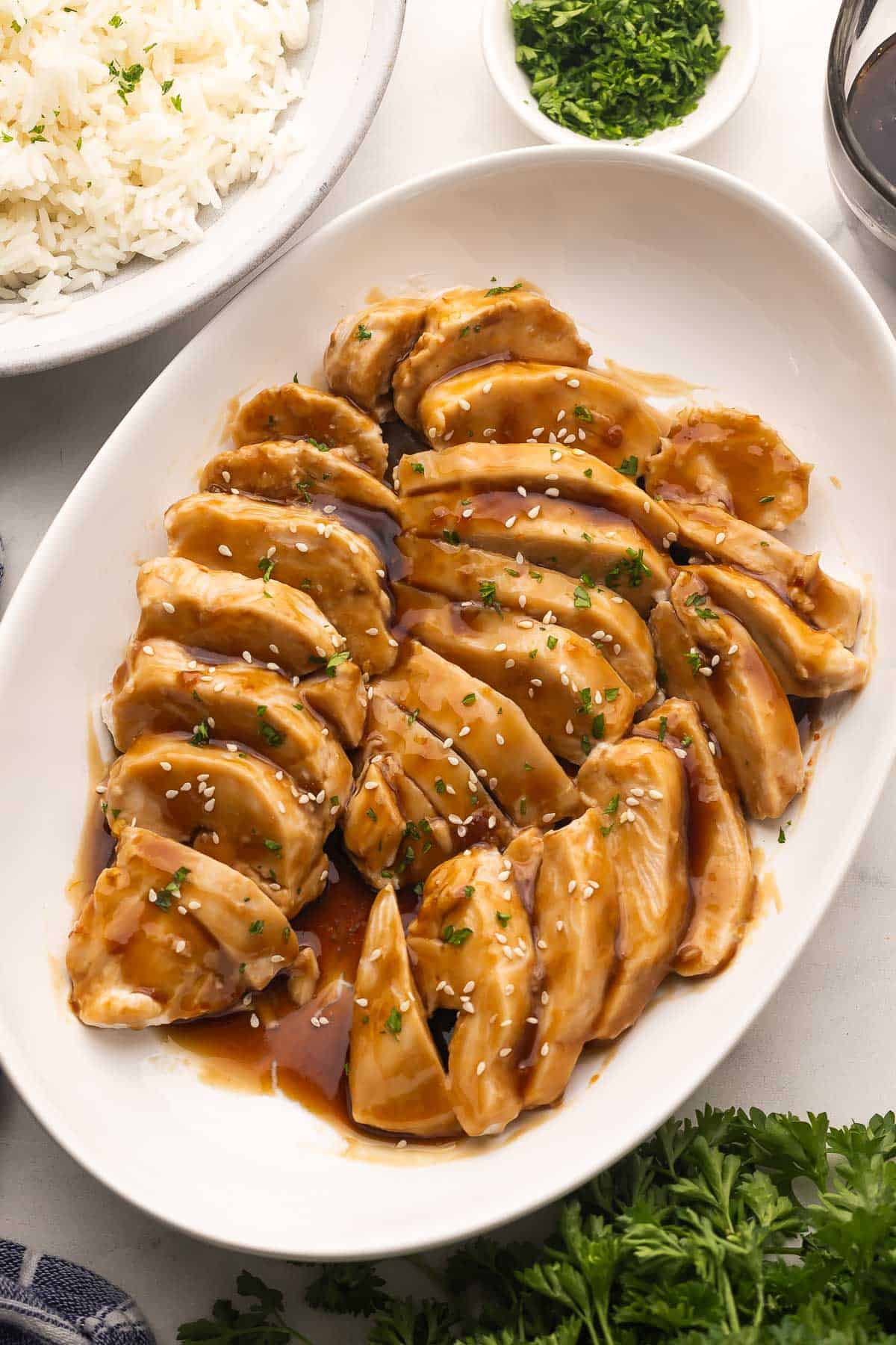 Slow Cooker Coconut Chicken cooks up tender in creamy coconut milk, then gets tossed in a sticky sweet-heat sauce. Serve it over rice or noodles for a bold, easy dinner! #slowcooker #dinner #recipe | chicken recipes | chicken breast | chicken dinner | dinner ideas | dinner recipes | slow cooker meals | crockpot chicken | easy dinners a white platter full of sweet and spicy coconut chicken yopped with chopped parsley.