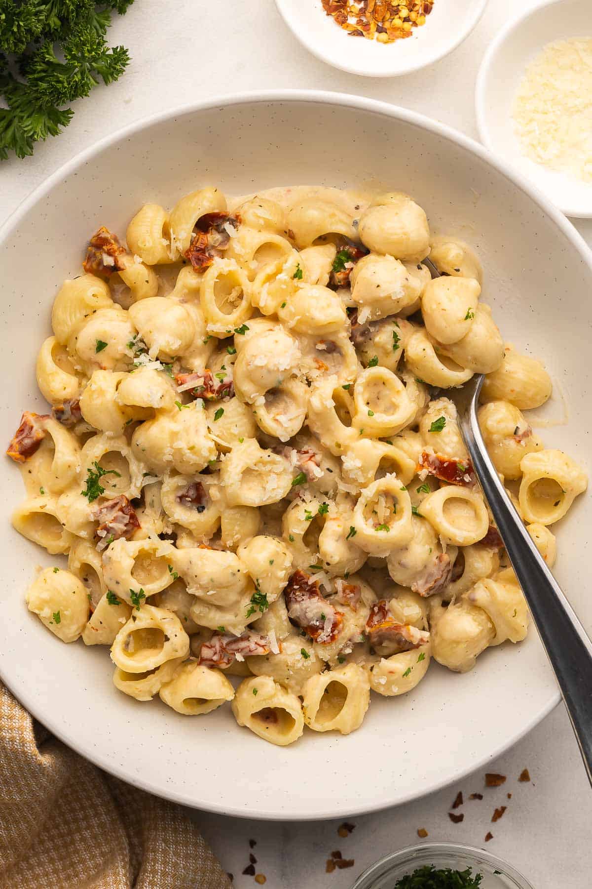 Sun Dried Tomato Pasta is a quick, creamy pasta dinner with garlic, Parmesan, and lots of sun dried tomato flavor. It's easy enough for weeknights and ready in 20 minutes! #pasta #dinner #recipe | easy pasta recipe | dinner ideas | sun dried tomatoes | sundried tomatoes | comfort food | dinner party a bowl of sun dried tomato pasta with a fork in it.