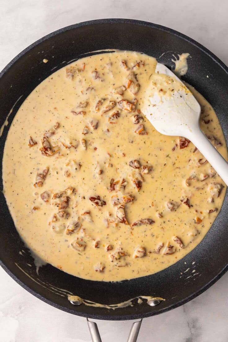 sun dried tomato sauce in black pan with white spatula.