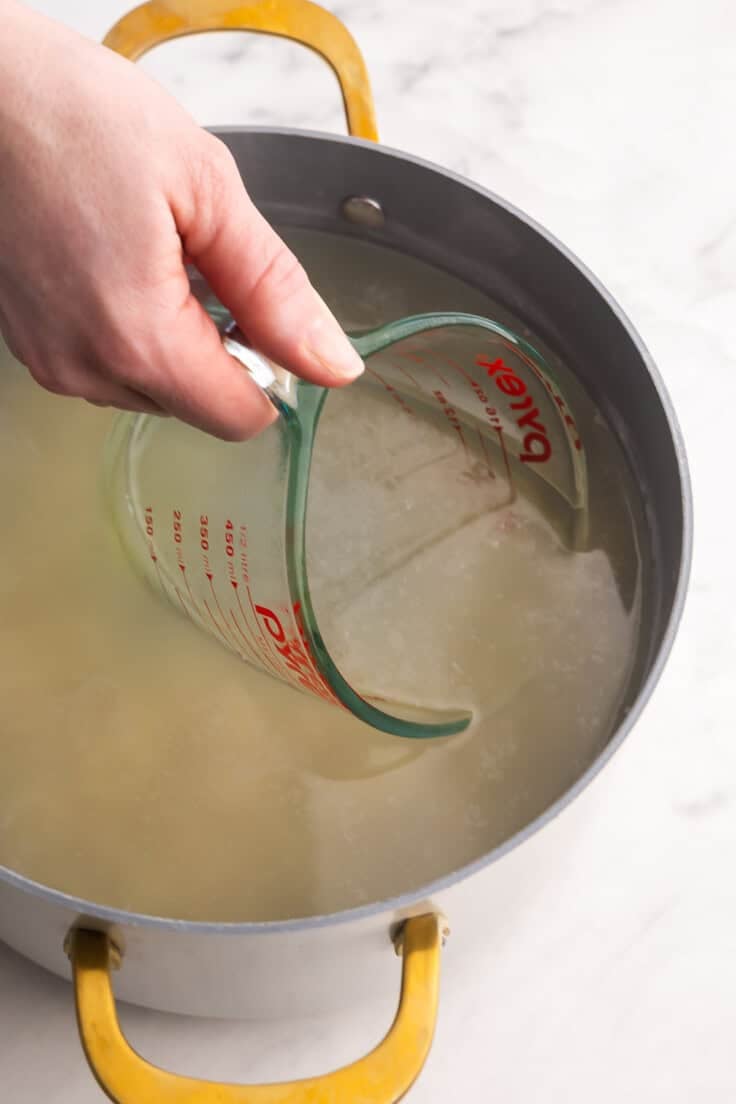 a measuring cup scooping pasta water out of white pot.