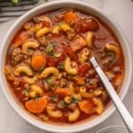 beef and tomato macaroni soup in a bowl topped with chopped parsley.
