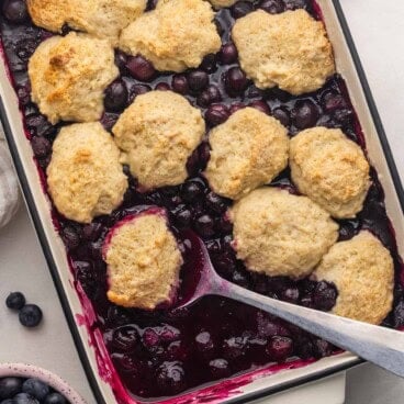 a large serving spoon in a pan of blueberry cobbler.