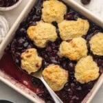 a large serving spoon in a pan of cherry cobbler.