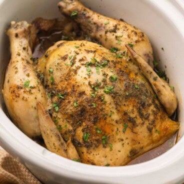 cooked crockpot whole chicken in white crockpot.