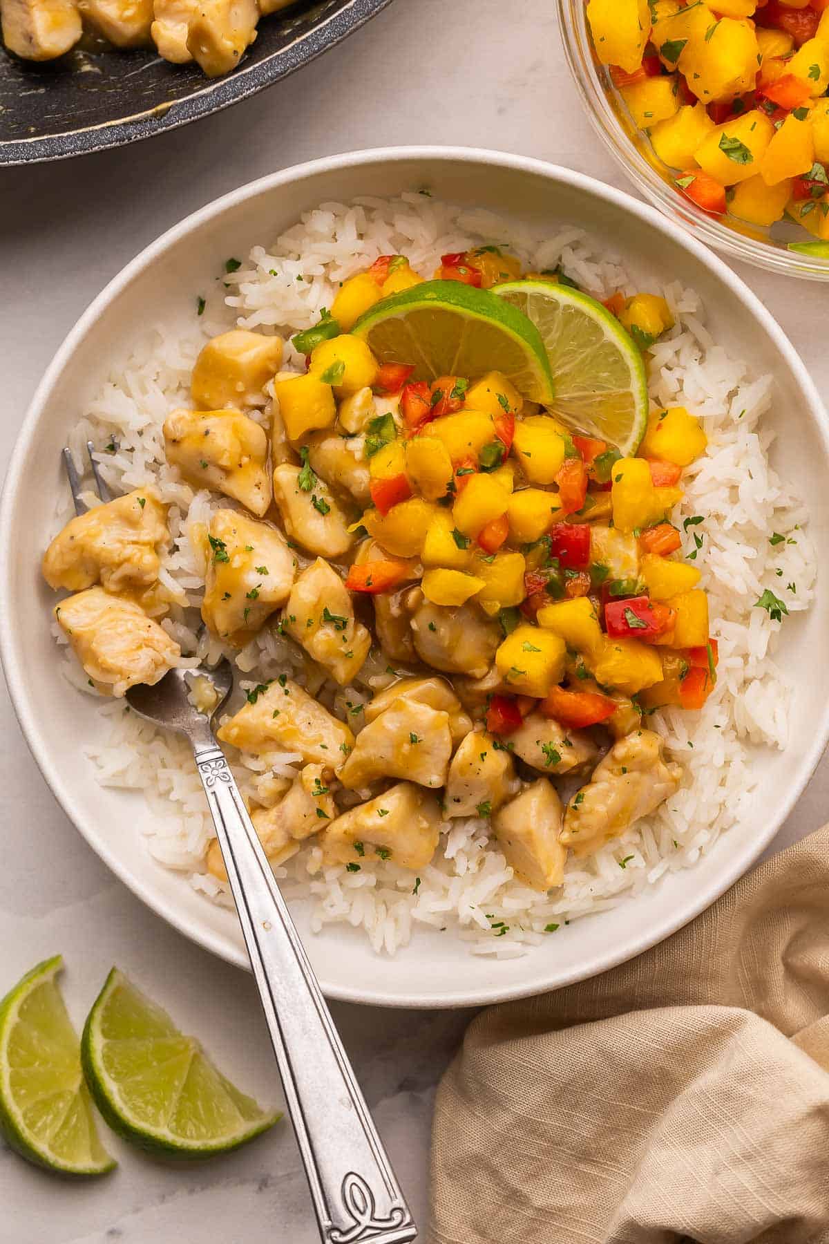 These Mango Chicken Rice Bowls with tender chicken breast, fluffy rice and homemade mango salsa are ready in just 35 minutes and perfect for weeknight dinners! #chicken #recipe #dinner | dinner ideas | dinner recipes | chicken breast recipes | chicken recipes | easy dinner ideas | healthy meals overhead image of mango salsa chicken rice bowls with a fork stuck in.