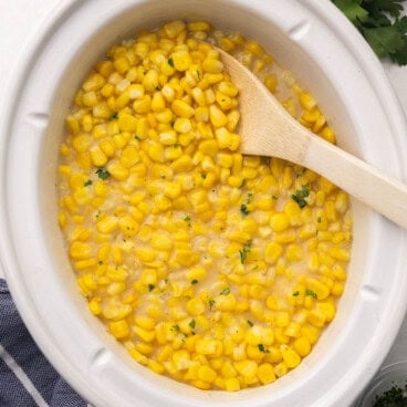 slow cooker filled with slow cooker creamed corn and wooden ladle.
